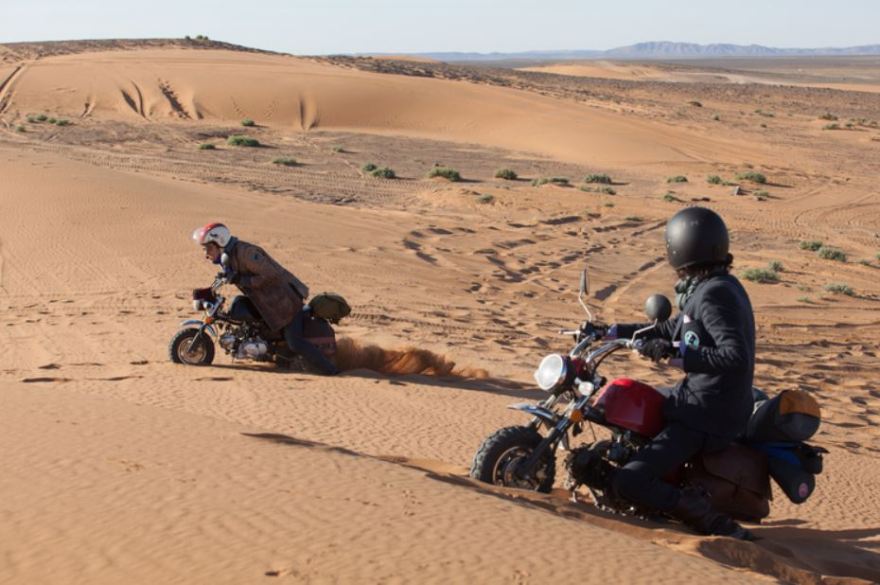 Two men pushing their way through a dessert on two tiny bikes