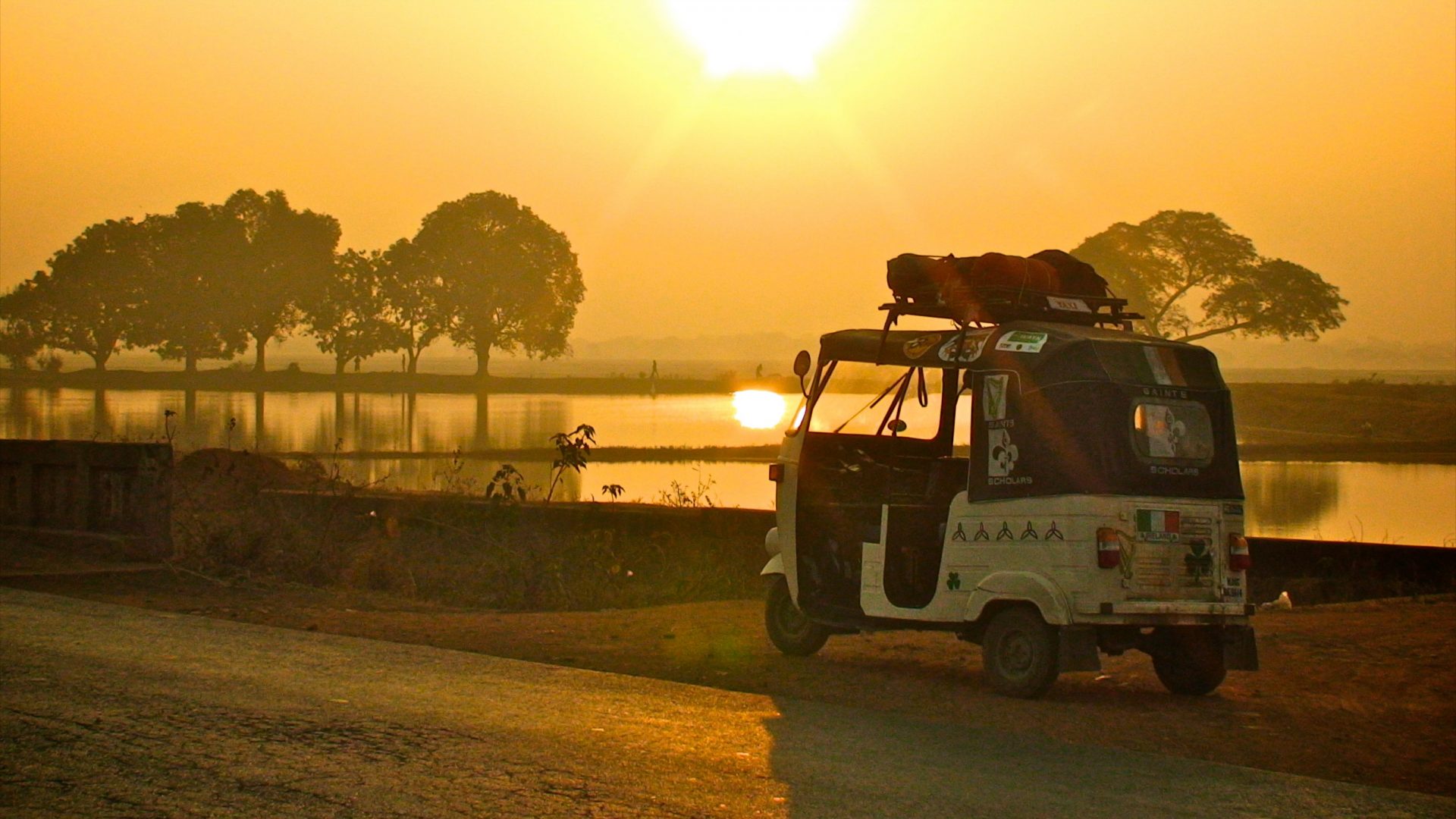 An auto rickshaw at the side of the road at sunrise.