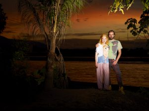 Vivienne and her husband Andreas pose next to a rainforest river at sunset.