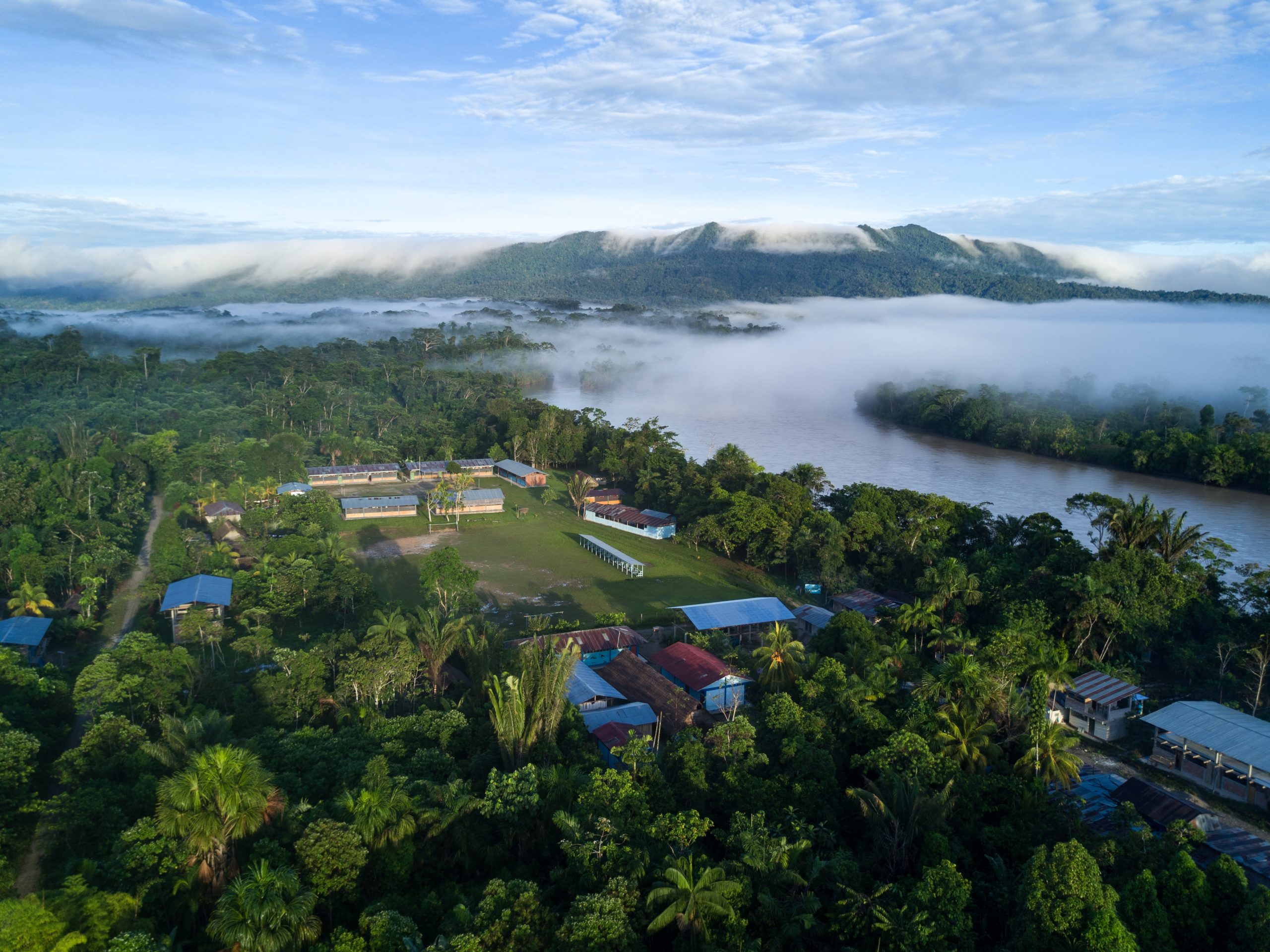 Aerial image of a village near a river with forested mountains in the background.