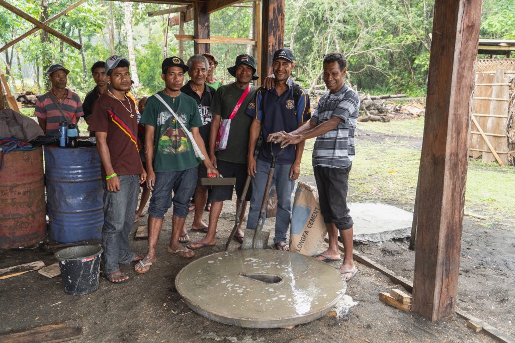 A group of young men stand behind their freshly poured concrete toilet.