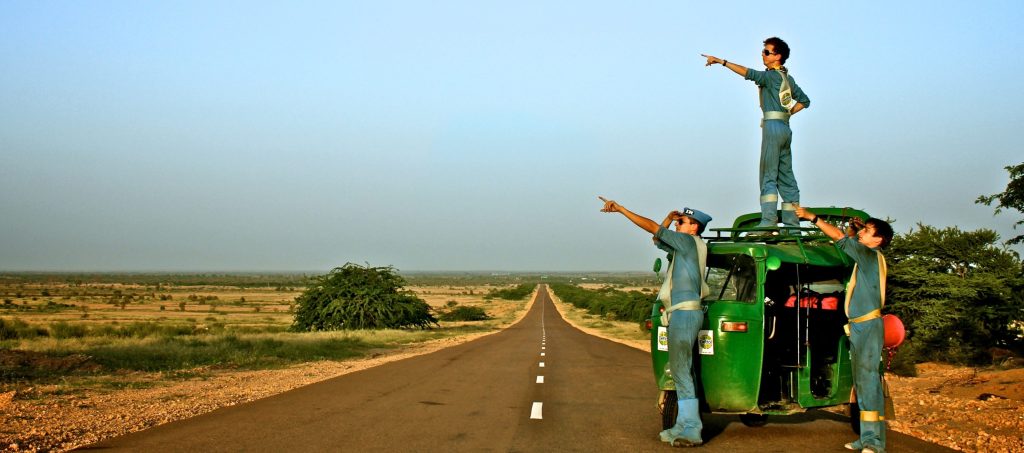 Three men stood next to a rickshaw, pointing to the sky on the open road