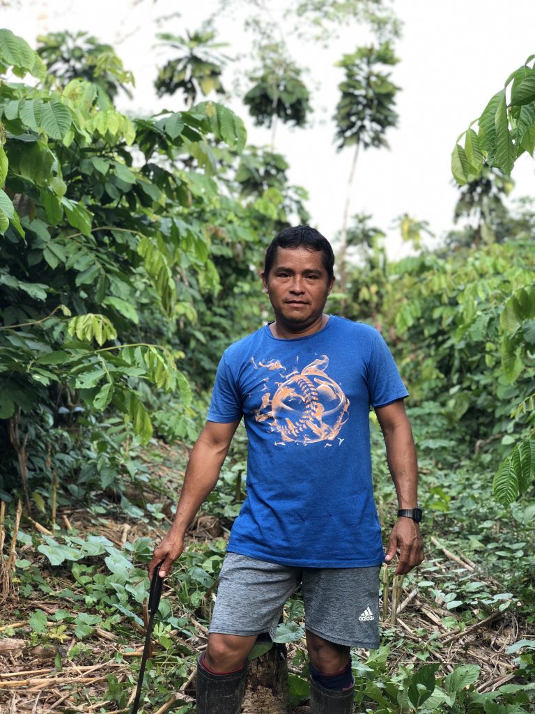 We see a man called Marin wearing a blue shirt and shorts in a small area of cleared rainforest. He looks content and happy with himself looking in to the camera holding a machete with its tip on the ground.