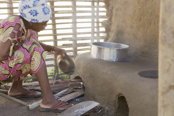 Lady wearing a bright pink patterns dress kneels next to fuel-efficient stove and fans it