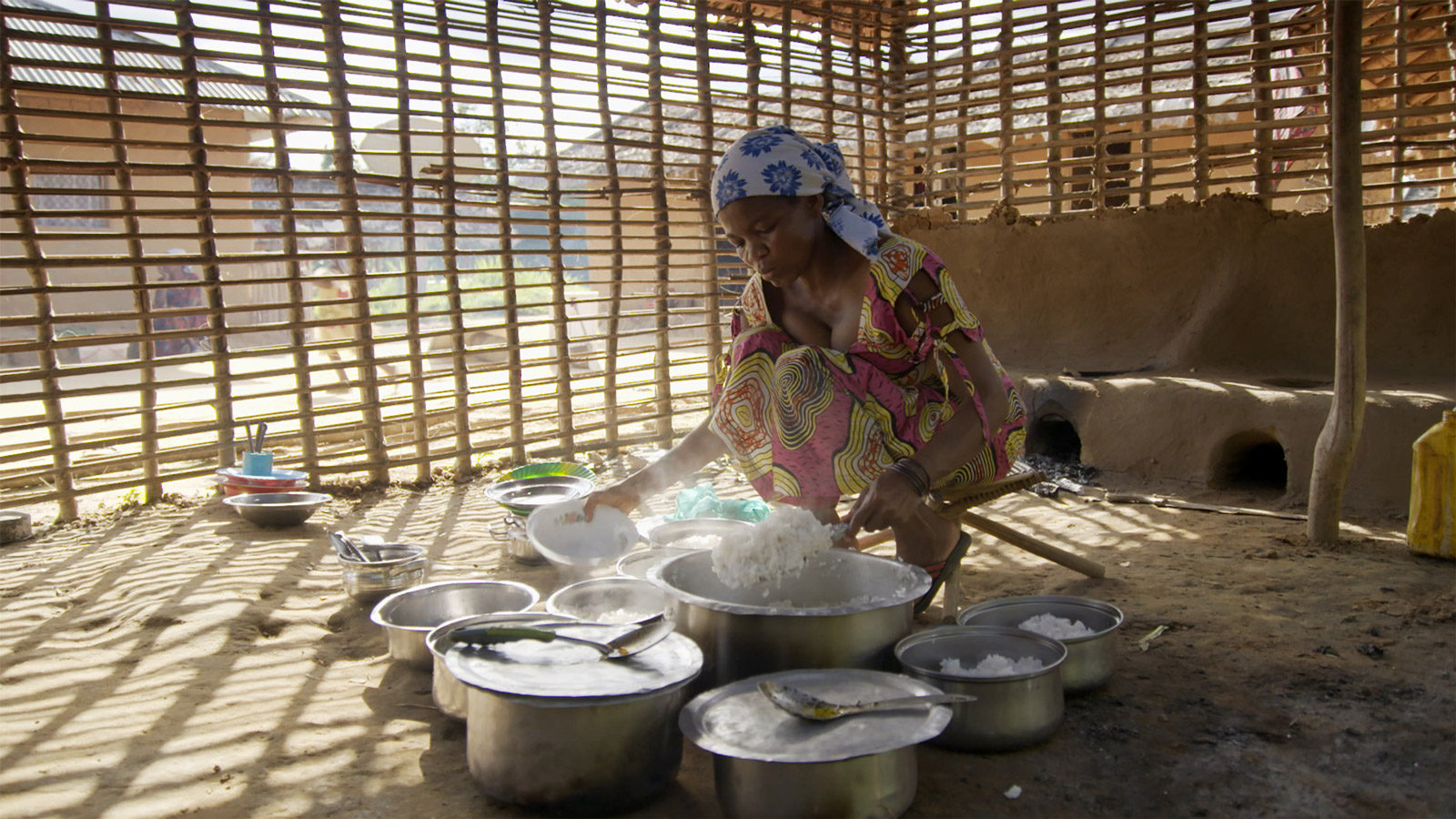 woman cooking on a stove on the ground surrounded by metal pots