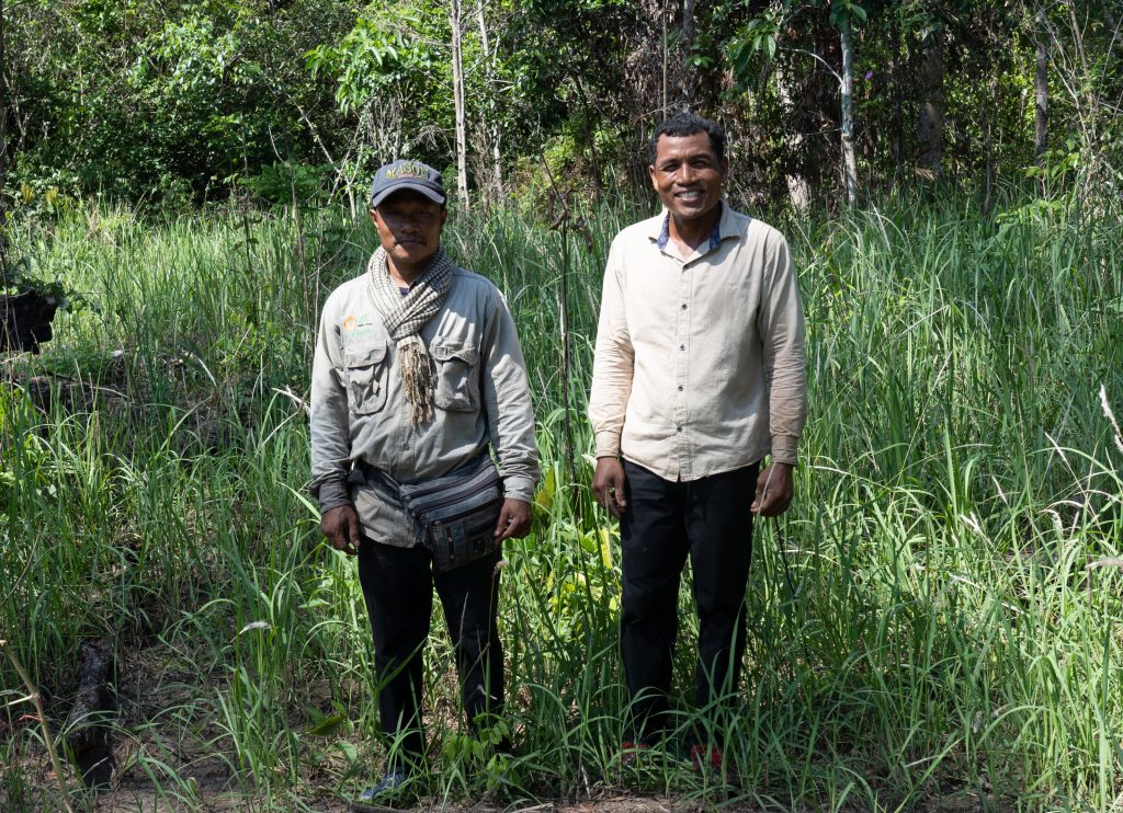 Crocodile wardens, smiling at the camera, whist standing in a grassy area of crocodile habitat.