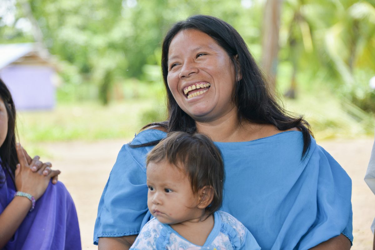 Portrait of Chabucca, she is laughing and wears a sky blue outfit and has a small child on her lap