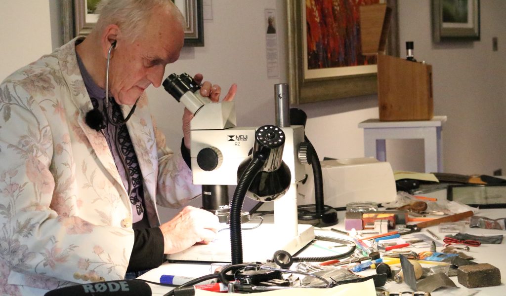 Graham looking though a microscope at his micro engraving. He is in his work station, surrounded by his engraving tools.