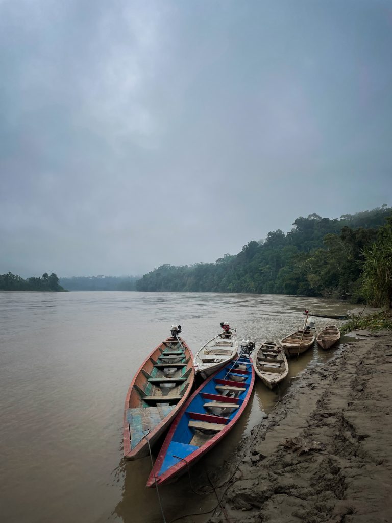 a collection of small boats are moored alongside a river bank under a moody sky.