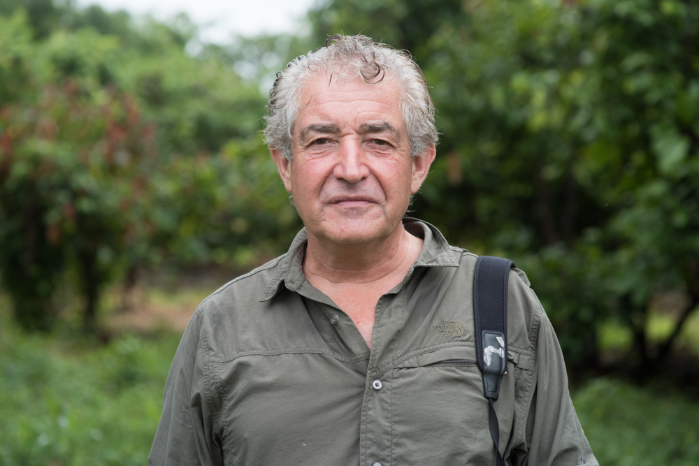 Portrait image of Tony Juniper, he is looking directly at the camera, wearing a green shirt with a camera over his shoulder