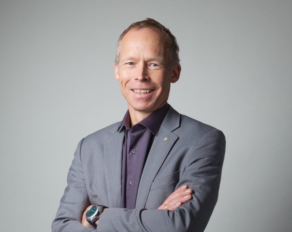 Portrait image of Johan Rockstrom, he is smiling and  has his arms folded. He wears a grey suit jacket