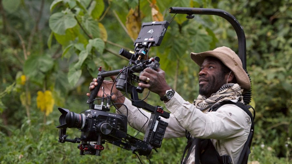 an action shot of Vianet Djenguet, he is in the forest and  holds a large camera