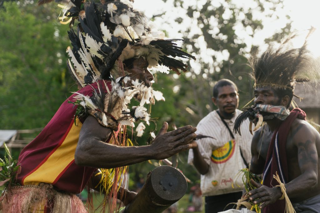 A man in traditional feathered headdress dances and plays a drum.