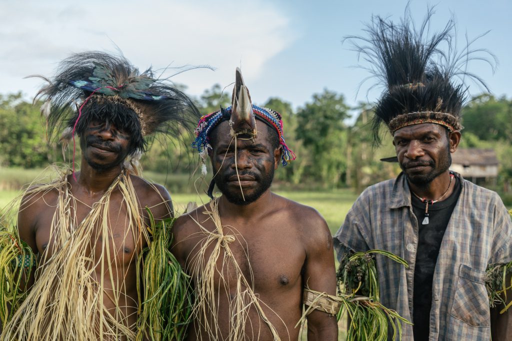 Three men pose in traditional feathered headgear.