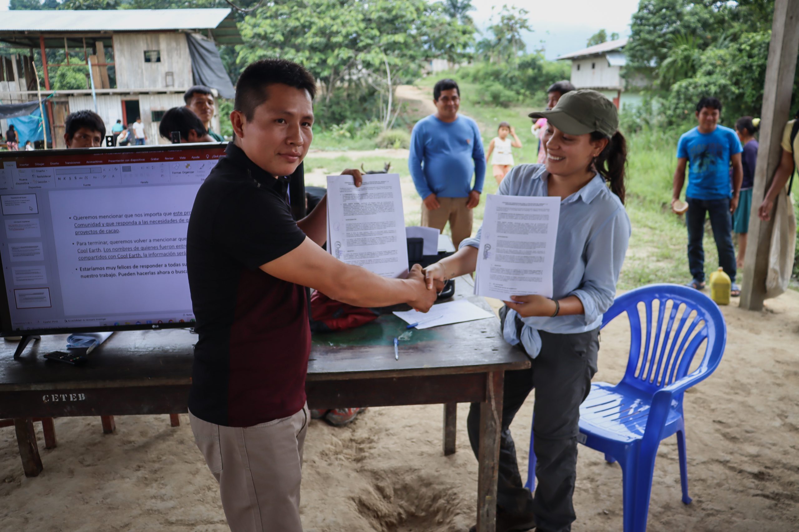 A signed document is held up to the camera over a handshake.