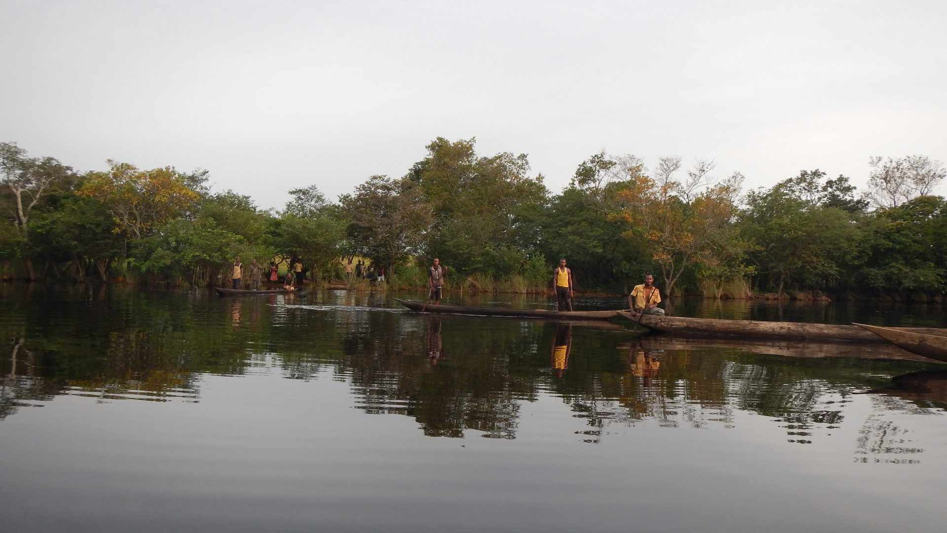 Local community forest concession members standing in canoes over the water, forest can be seen in the background.