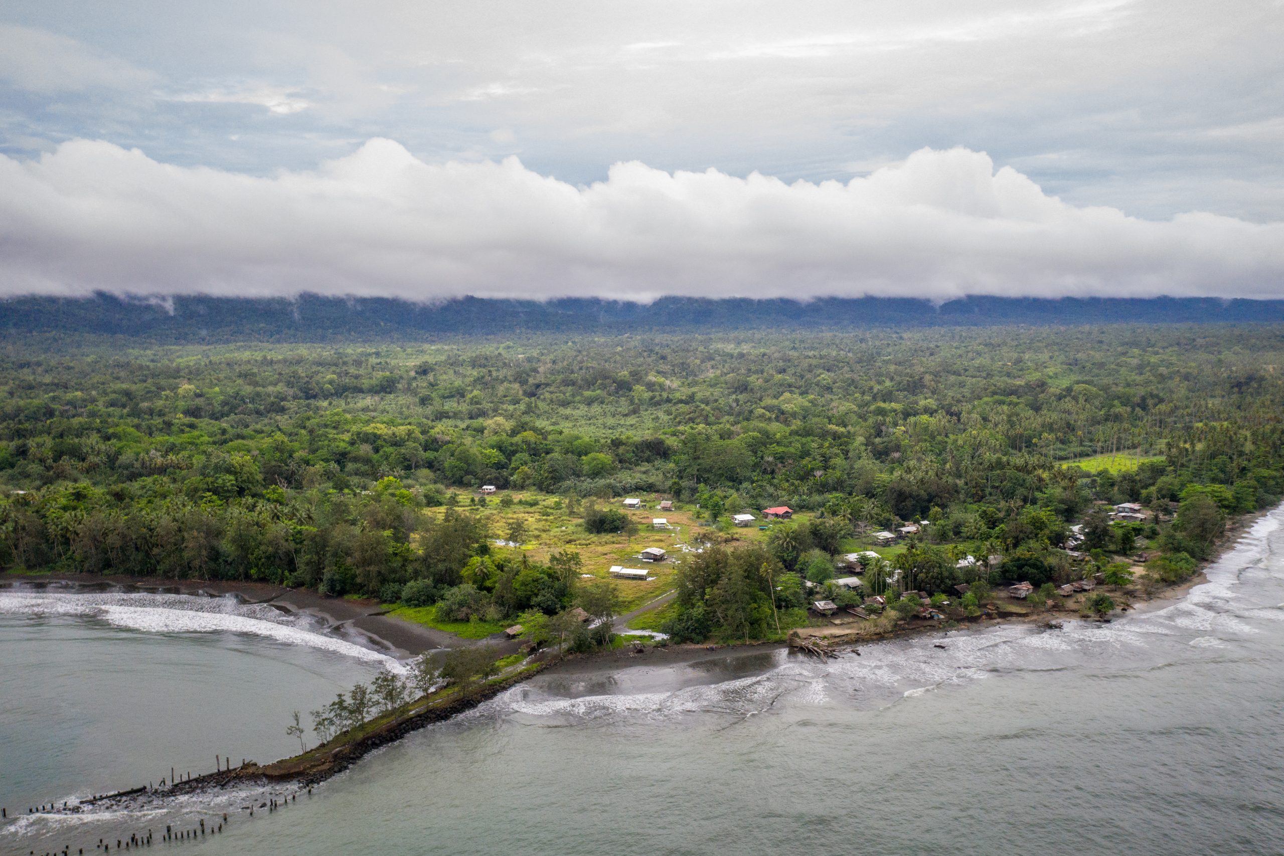 Aerial view of Gadaisu Village, PNG. Dense rainforest wraps around the village before it meets the sea.