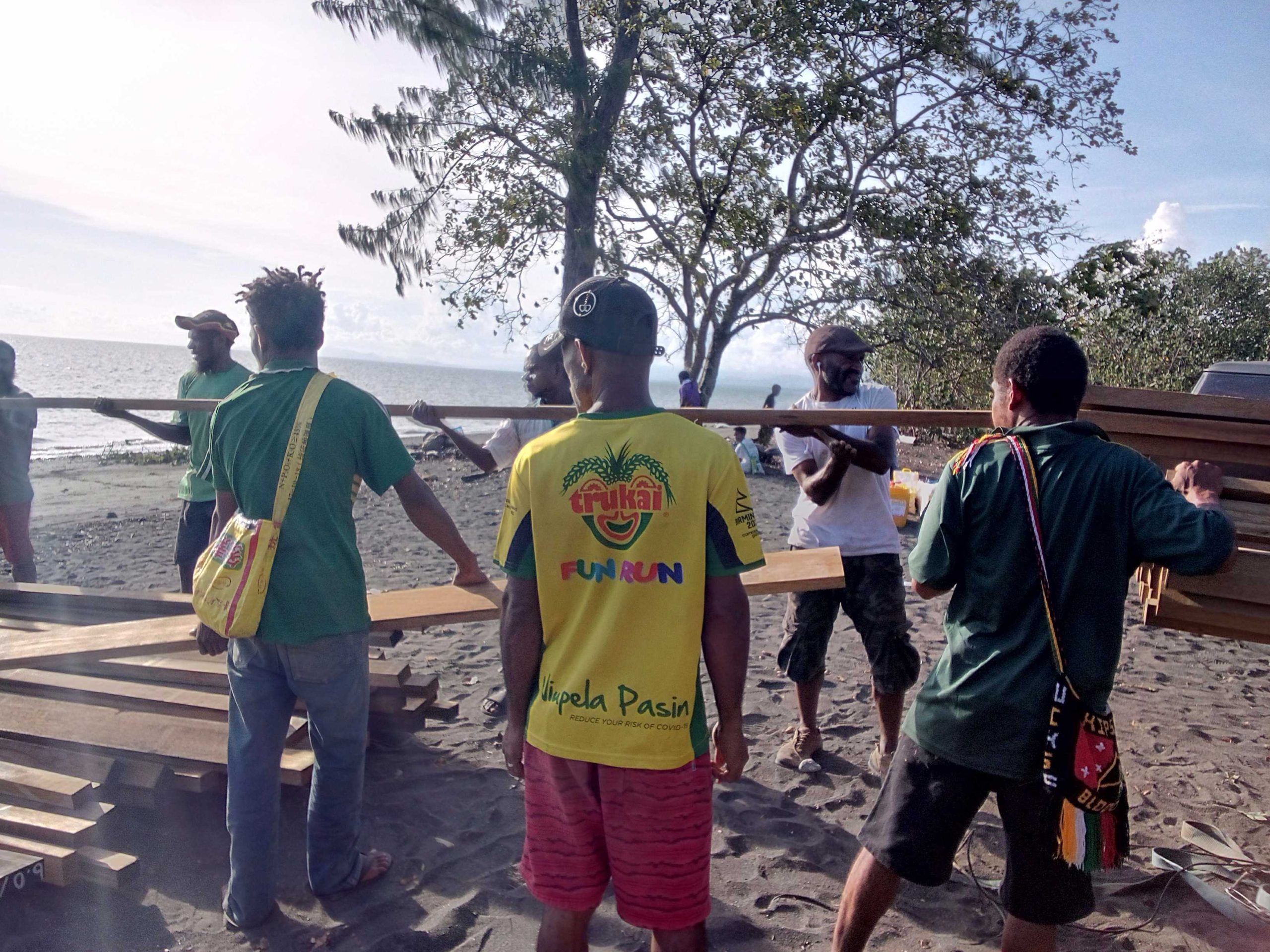 Eight men help with the loading of timber onto a pick up truck.