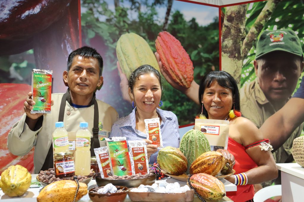 Leonel, Flor and Cemilia team members of the chocolate factory smile at the camera and proudly hold up their Chikaun products